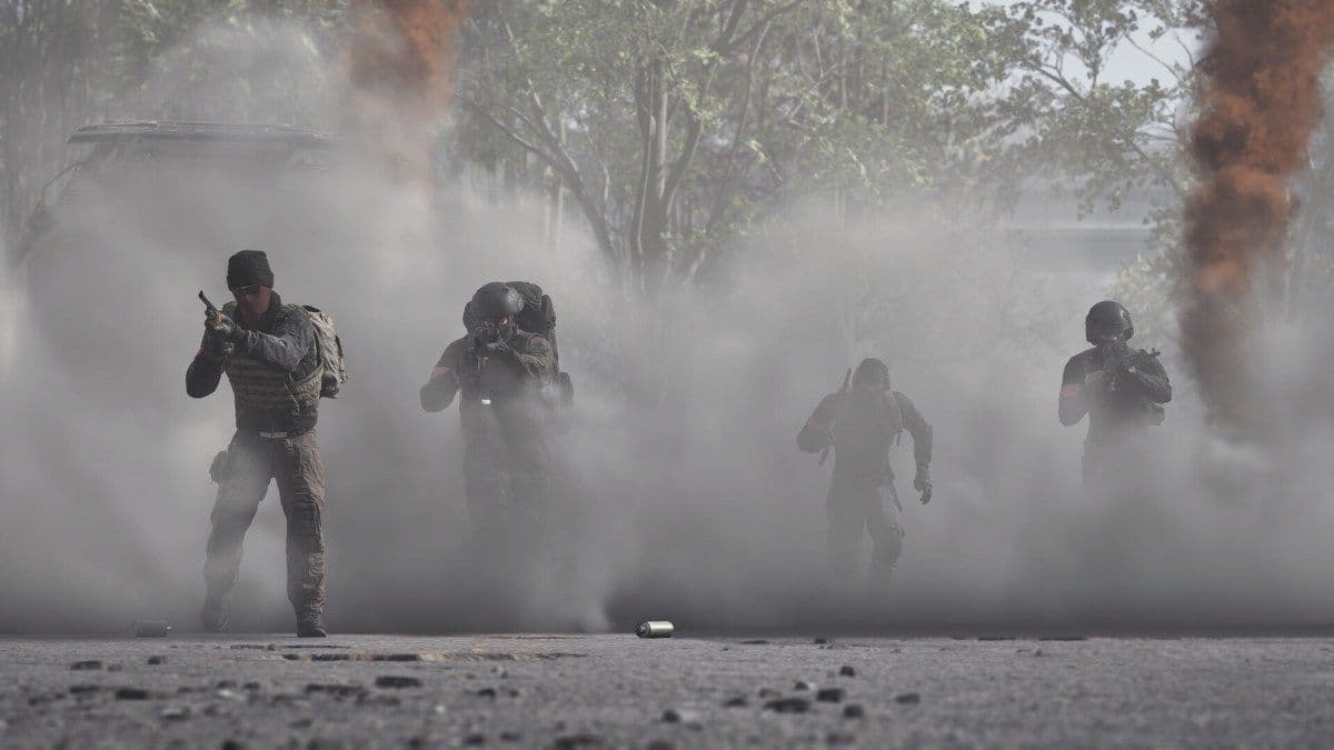 Four soldiers advance through a wall of smoke with flares burning behind them in WARDOGS