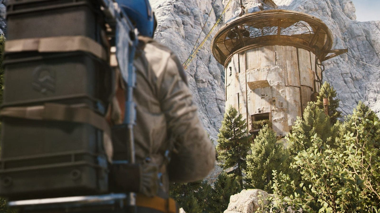 A Raider with a large backpack looks up at a weathered round tower on a pine-covered mountainside